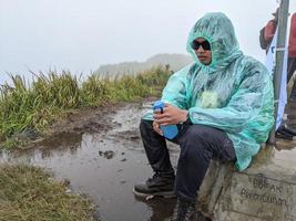 Man reach peak of mountain when rainy day with foggy vibes. The photo is suitable to use for adventure content media, nature poster and forest background.