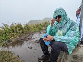 hombre alcanzar pico de montaña cuando lluvioso día con brumoso vibras. el foto es adecuado a utilizar para aventuras contenido medios de comunicación, naturaleza póster y bosque antecedentes.