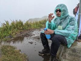 hombre alcanzar pico de montaña cuando lluvioso día con brumoso vibras. el foto es adecuado a utilizar para aventuras contenido medios de comunicación, naturaleza póster y bosque antecedentes.