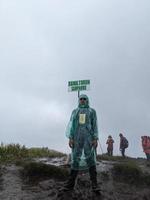 Man reach peak of mountain when rainy day with foggy vibes. The photo is suitable to use for adventure content media, nature poster and forest background.