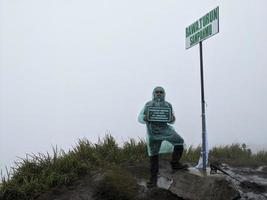Man reach peak of mountain when rainy day with foggy vibes. The photo is suitable to use for adventure content media, nature poster and forest background.