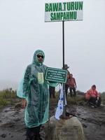 Man reach peak of mountain when rainy day with foggy vibes. The photo is suitable to use for adventure content media, nature poster and forest background.