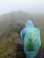 Man reach peak of mountain when rainy day with foggy vibes. The photo is suitable to use for adventure content media, nature poster and forest background.