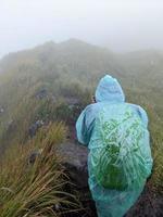 hombre alcanzar pico de montaña cuando lluvioso día con brumoso vibras. el foto es adecuado a utilizar para aventuras contenido medios de comunicación, naturaleza póster y bosque antecedentes.