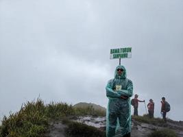 Man reach peak of mountain when rainy day with foggy vibes. The photo is suitable to use for adventure content media, nature poster and forest background.