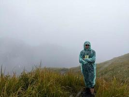 hombre alcanzar pico de montaña cuando lluvioso día con brumoso vibras. el foto es adecuado a utilizar para aventuras contenido medios de comunicación, naturaleza póster y bosque antecedentes.