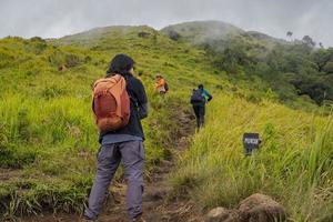 Man hiking to the top mountain, with Savana track and cloudy vibes. The photo is suitable to use for adventure content media, nature poster and forest background.