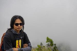 Man hiking to the top mountain, with Savana track and cloudy vibes. The photo is suitable to use for adventure content media, nature poster and forest background.