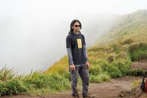 Man hiking to the top mountain, with Savana track and cloudy vibes. The photo is suitable to use for adventure content media, nature poster and forest background.