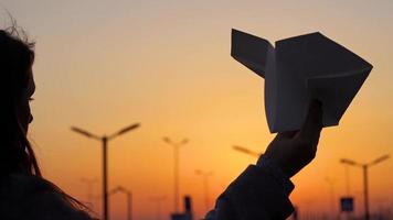 donna lancia carta aereo contro tramonto sfondo. concetto di volendo per partire su vacanza o viaggio video