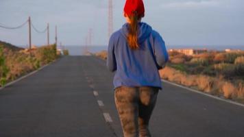 mujer carreras a lo largo el abandonado asfalto la carretera a puesta de sol. montañas en el antecedentes. video