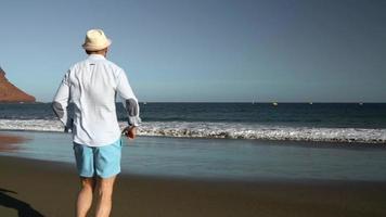 gelukkig Mens loopt langs de oceaan strand Bij zonsondergang. concept van zorgeloos modern leven. tenerife, Canarisch eilanden. langzaam beweging video