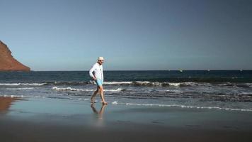 Happy man runs along the ocean beach at sunset. Concept of carefree modern life. Tenerife, Canarian Islands. Slow motion video