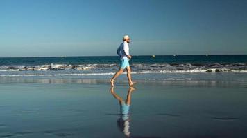 gelukkig Mens loopt langs de oceaan strand Bij zonsondergang. concept van zorgeloos modern leven. tenerife, Canarisch eilanden. langzaam beweging video