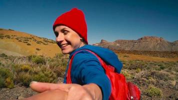 seguir yo - contento joven mujer en rojo sombrero con mochila tracción tipo mano. mano en mano caminando lanzar el teide nacional video