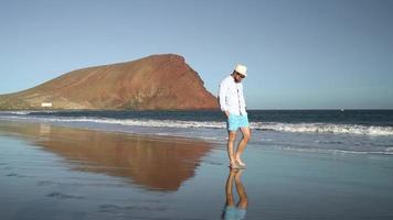 gelukkig Mens loopt langs de oceaan strand Bij zonsondergang. concept van zorgeloos modern leven. tenerife, Canarisch eilanden. langzaam beweging video