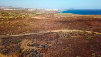 aereo Visualizza di un' donna escursioni a piedi lungo un' vulcanico superficie vicino il oceano costa, tenerife, canarino isole, Spagna video