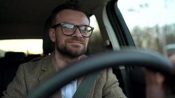 Satisfied bearded man driving a car down the street in sunny weather video