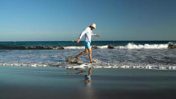 Happy man runs along the ocean beach at sunset. Concept of carefree modern life. Tenerife, Canarian Islands. Slow motion video