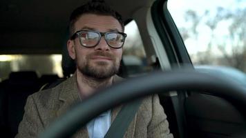 Satisfied bearded man driving a car down the street in sunny weather video