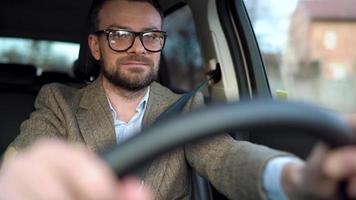 Satisfied bearded man driving a car down the street in sunny weather video