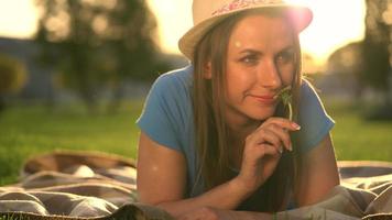 Girl with a dandelion in her hands relaxes lying down on a blanket in the park at sunset video