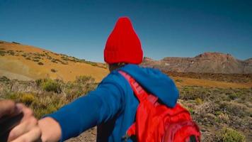 suivre moi - content Jeune femme dans rouge chapeau avec sac à dos tirant gars main. main dans main en marchant jeter le teide nationale video