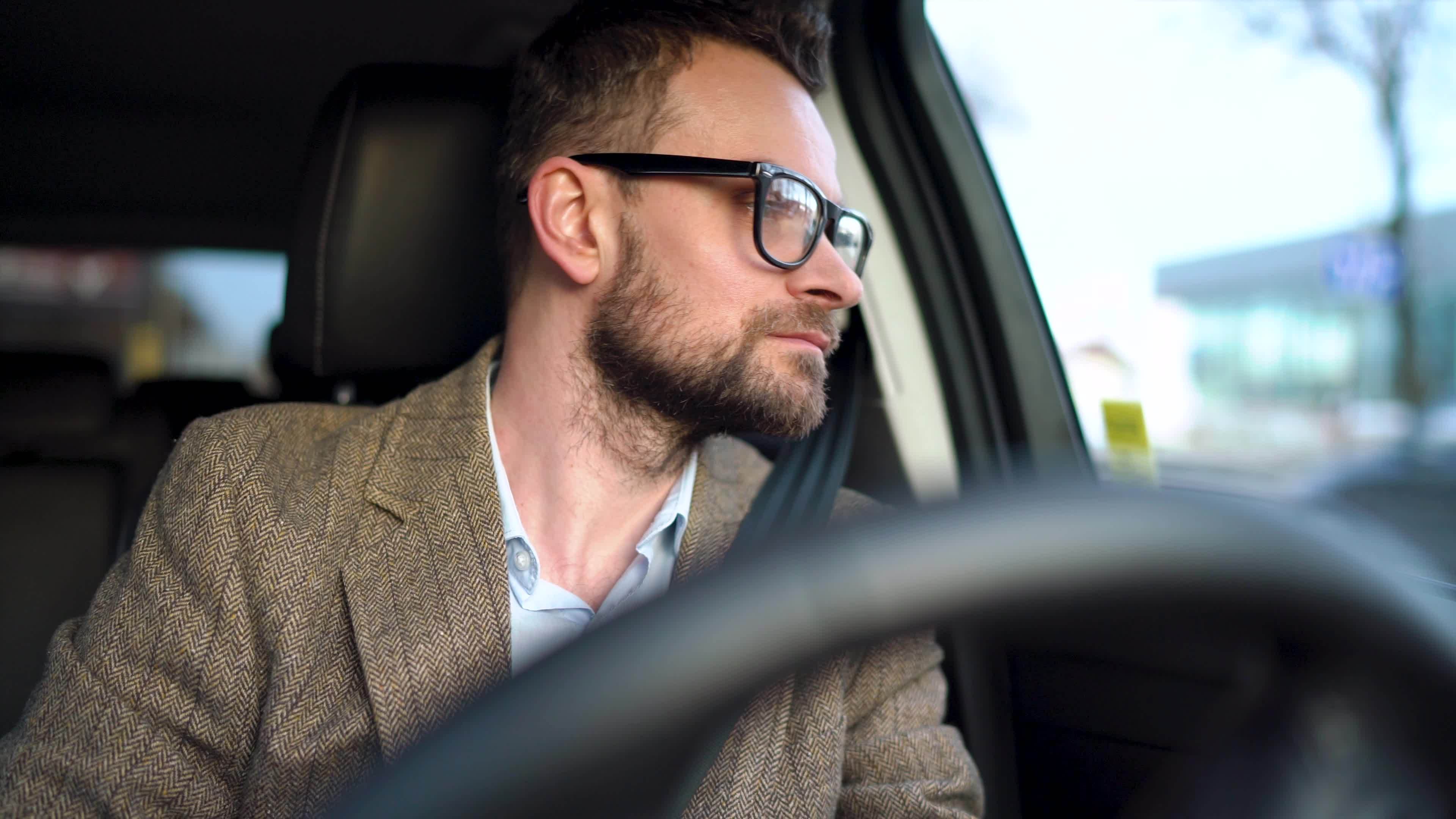 Satisfied bearded man driving a car down the street in sunny weather ...