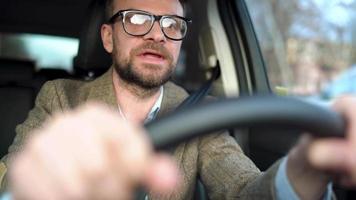 satisfecho barbado hombre conducción un coche abajo el calle en soleado clima video