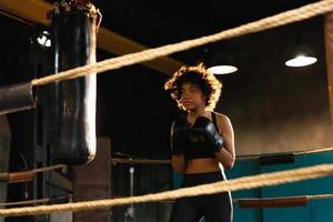 mujer yo defensa niña fuerza. africano americano mujer combatiente formación puñetazos en boxeo anillo. sano fuerte niña puñetazos boxeo bolsa. formación día en boxeo gimnasia. fuerza ajuste cuerpo rutina de ejercicio capacitación. foto