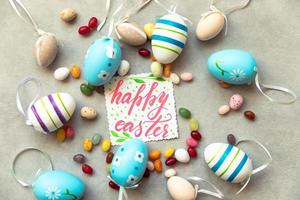 Happy Easter concept. Preparation for holiday. Easter eggs Inscription HAPPY EASTER letters candy chocolate eggs and jellybean sweets on concrete stone grey background. Flat lay top view copy space. photo