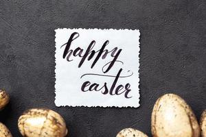 Happy Easter concept. Preparation for holiday. Golden Easter eggs Inscription HAPPY EASTER letters text on grunge scratched dark black shale background. Flat lay top view copy space. photo