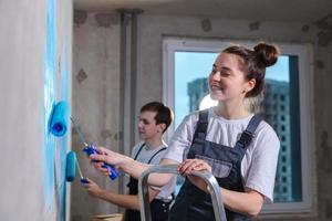 Couple in new home during repair works painting wall together. Happy family holding paint roller painting wall with blue color paint in new house. Home renovation DIY renew home concept. photo