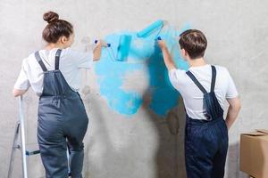 Couple in new home during repair works painting wall together. Happy family holding paint roller painting wall with blue color paint in new house. Home renovation DIY renew home concept. photo