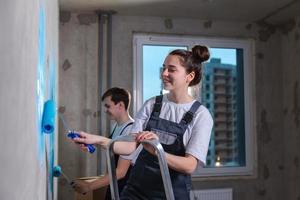 Couple in new home during repair works painting wall together. Happy family holding paint roller painting wall with blue color paint in new house. Home renovation DIY renew home concept. photo