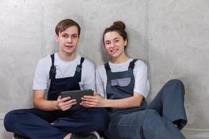 House DIY renovation concept. Young happy couple sitting on floor looking home repair plan in tablet indoors. Woman showing to man plan interior design online. Couple in new home during repair works. photo