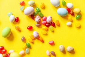 Happy Easter concept. Preparation for holiday. Easter candy chocolate eggs and jellybean sweets isolated on trendy yellow background. Simple minimalism flat lay top view copy space. photo