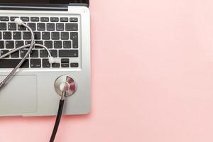 Stethoscope keyboard laptop computer isolated on pink background. Modern medical Information technology and sofware advances concept. Computer and gadget diagnostics and repair photo