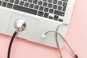 Stethoscope keyboard laptop computer isolated on pink background. Modern medical Information technology and sofware advances concept. Computer and gadget diagnostics and repair photo