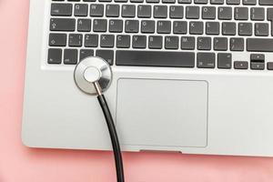 Stethoscope keyboard laptop computer isolated on pink background. Modern medical Information technology and sofware advances concept. Computer and gadget diagnostics and repair photo