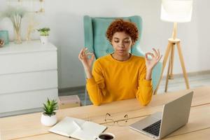 No stress keep calm. Mindful african businesswoman practices breathing exercises at home office. Peaceful young woman at workplace enjoy yoga eyes closed hands in chin mudra gesture, Office meditation photo