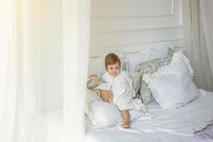 linda pequeño niña saltando en blanco cama foto