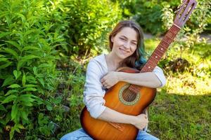 joven mujer sentado en césped y jugando guitarra foto