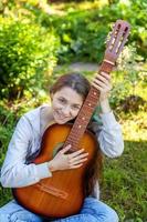 Young woman sitting in grass and playing guitar photo