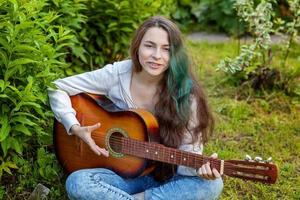 Young woman sitting in grass and playing guitar photo