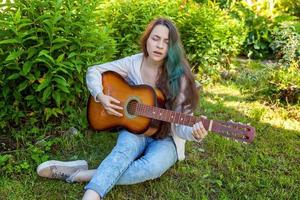 Young woman sitting in grass and playing guitar photo