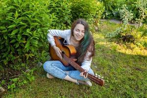 Young woman sitting in grass and playing guitar photo