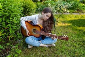 Young woman sitting in grass and playing guitar photo