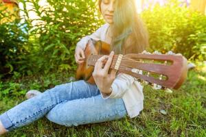 joven mujer sentado en césped y jugando guitarra foto