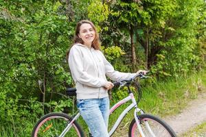 mujer joven montando en bicicleta en el parque de la ciudad de verano al aire libre. gente activa chica hipster relajarse y andar en bicicleta foto